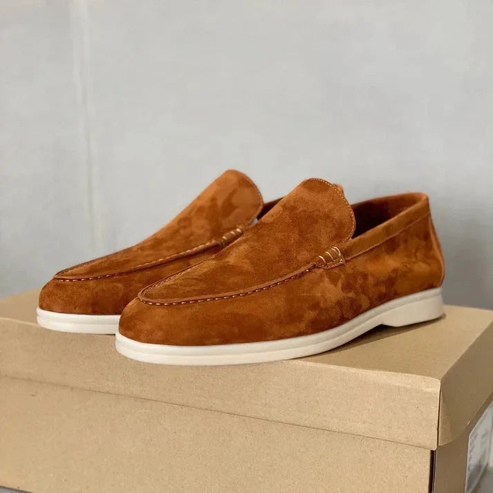 Side profile of black suede loafers with white contrast sole beside their shoe box