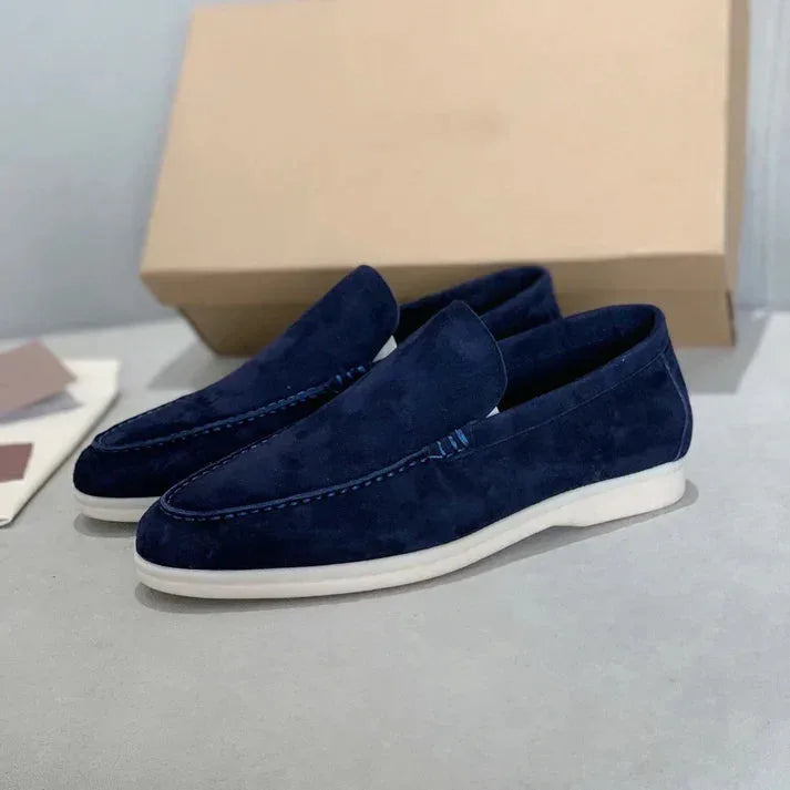 Side profile of dusty blue suede loafers with white sole shown next to the shoe box