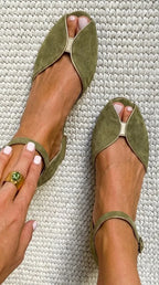 Close-up top view of sage green suede flat sandals with gold edge trim and slim ankle strap