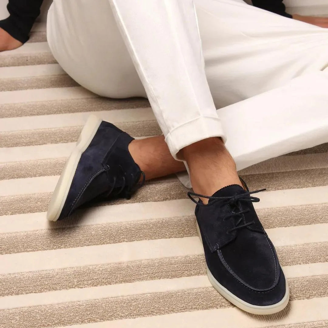 Side profile of navy suede lace-up shoes with a moc-toe stitch and a cream rubber sole
