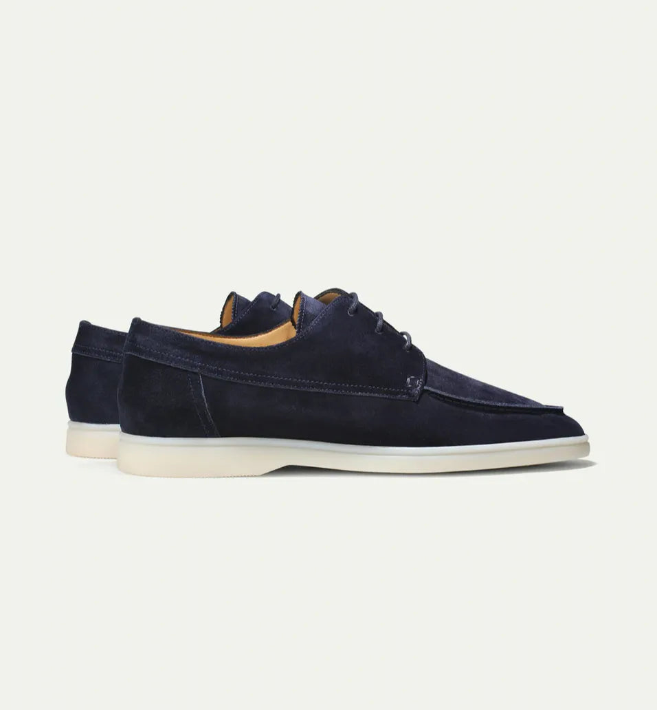 Rear-angled view of navy suede lace-up shoes showing the heel seam and cream outsole