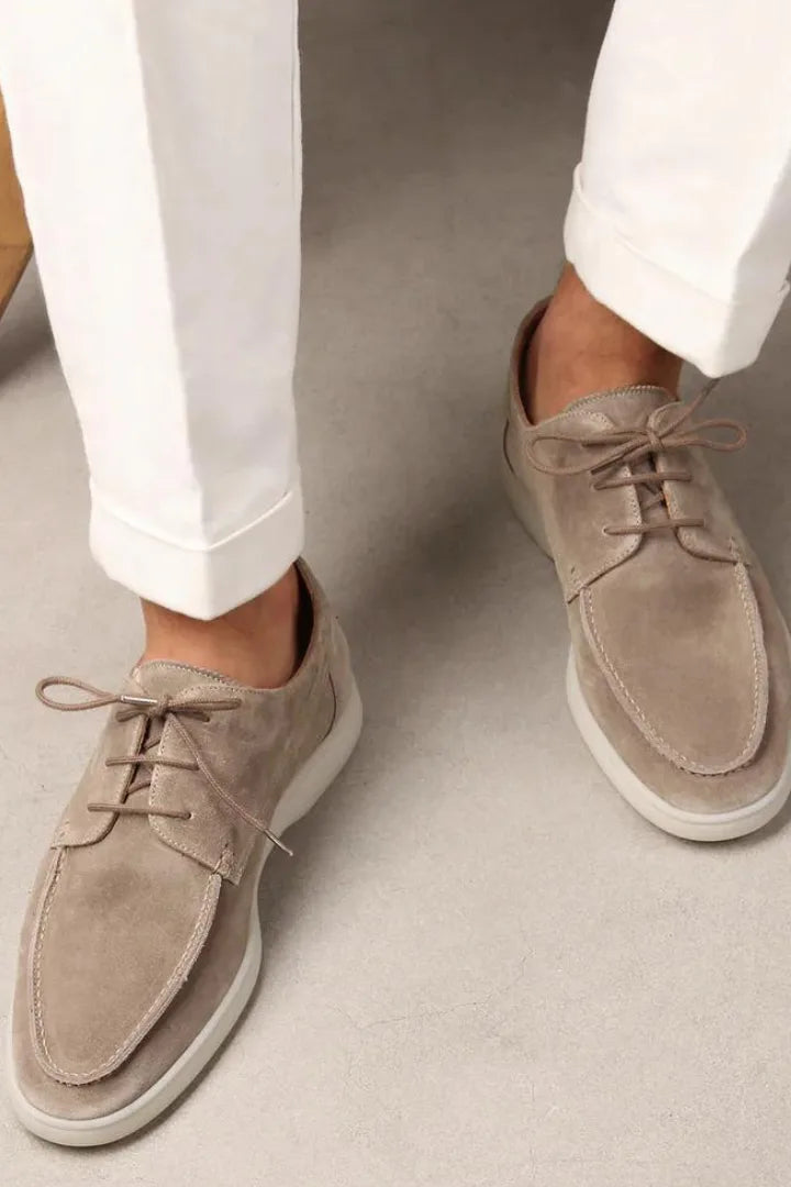 Man wearing beige suede lace-up shoes with white cuffed trousers, standing on a concrete floor