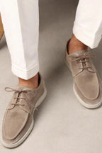 Man wearing beige suede lace-up shoes with white cuffed trousers, standing on a concrete floor