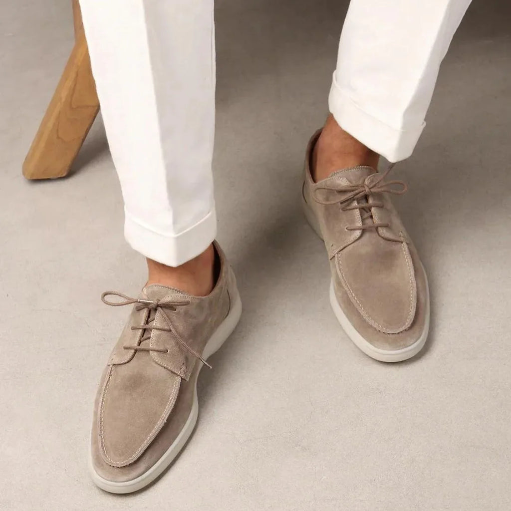 Model wearing beige suede lace-up shoes with white cuffed pants, standing on a light floor