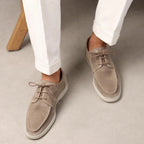Model wearing beige suede lace-up shoes with white cuffed pants, standing on a light floor