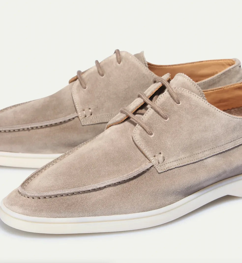 Close-up angled shot of beige suede shoes showing the apron stitching and lace detail