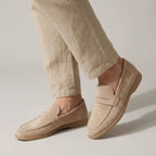 Front angled view of cream suede penny loafers showing the stitched apron toe and tan gum outsole