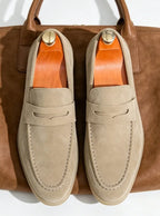 Overhead flat lay of a beige suede penny loafer pair resting on a tan leather tote bag