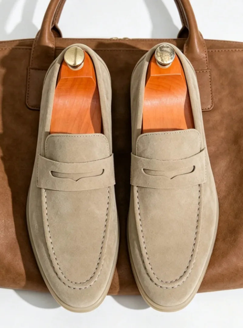 Overhead flat lay of a beige suede penny loafer pair resting on a tan leather tote bag