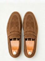 Top-down shot of tan suede penny loafers fitted with wooden shoe trees and brass knobs