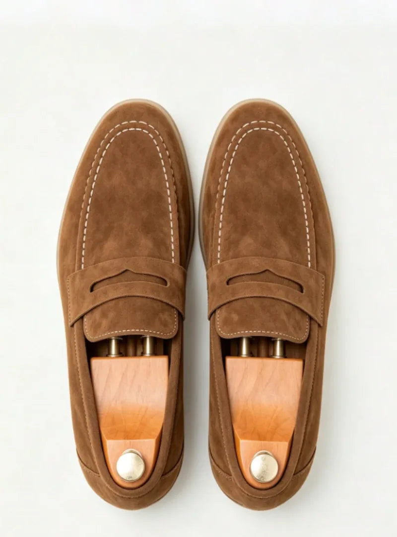 Top-down shot of tan suede penny loafers fitted with wooden shoe trees and brass knobs