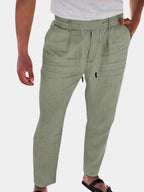 Close-up front view of sage green linen-blend pants with drawstring waist and pleated pockets, worn with sandals