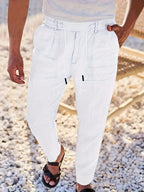 Close-up of white linen-blend pants highlighting the drawstring waistband and tapered leg against a stone pathway