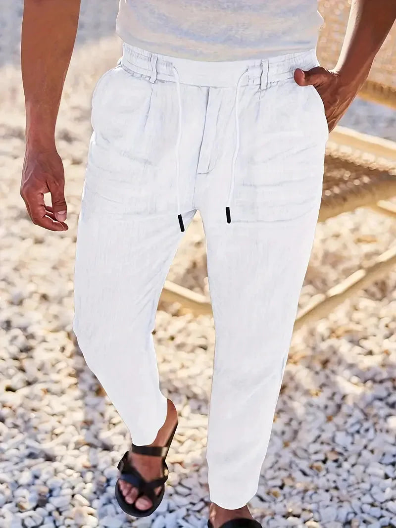 Close-up of white linen-blend pants highlighting the drawstring waistband and tapered leg against a stone pathway