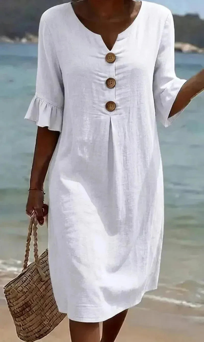 Close-up of white textured button-front dress with ruffled sleeves worn at the beach, buttons and pleat detail visible