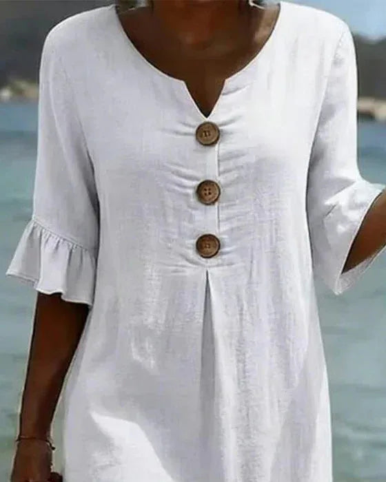 Detailed close-up of the V-neckline, wooden buttons and front pleat on the white textured dress