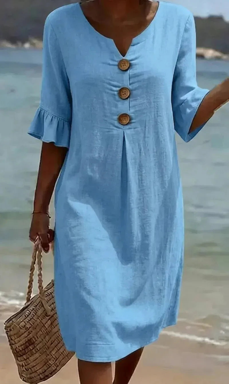Front close-up of light blue textured button dress with ruffled half sleeves against an ocean backdrop