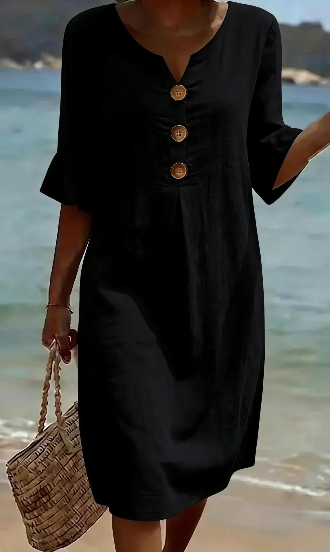 Front view of black textured shift dress with wooden buttons and ruffled sleeves on a beach setting
