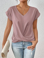 Close view of a dusty pink V-neck top with twist-front hem detail and cap sleeves, paired with ripped jeans