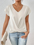 Off-white V-neck top highlighting the smooth drape of the crossover hem and rolled sleeve edges