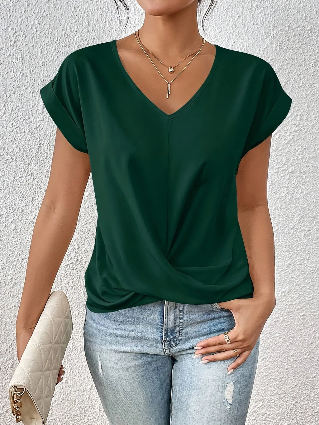Forest green V-neck top with twist hem, modelled against a textured white wall background