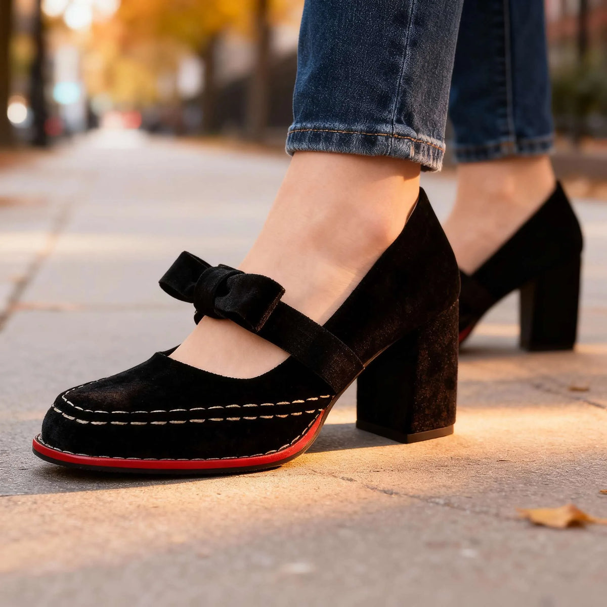 Black velvet mary jane heels with bow strap and red-trimmed sole worn with cuffed jeans