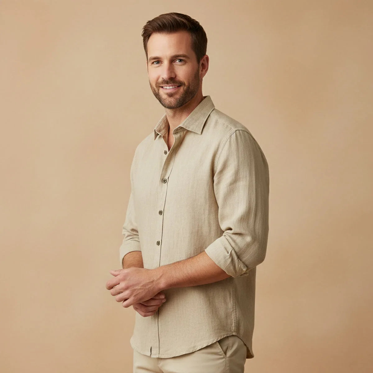 Man wearing khaki linen shirt with sleeves rolled, standing against a tan backdrop