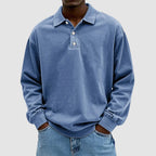 Man wearing a blue washed long-sleeve polo jumper with turn-down collar and two-button placket, hands in jean pockets