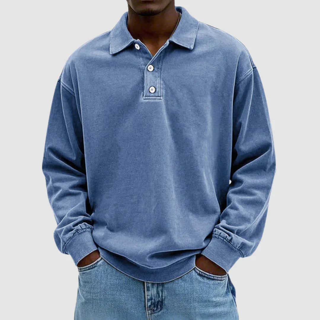 Man wearing a blue washed long-sleeve polo jumper with turn-down collar and two-button placket, hands in jean pockets