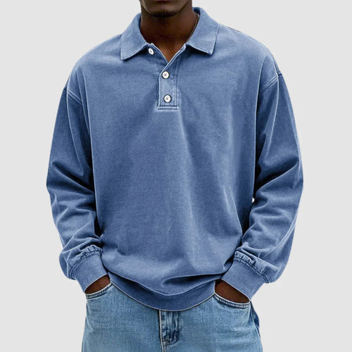 Man wearing a blue washed long-sleeve polo jumper with turn-down collar and two-button placket, hands in jean pockets