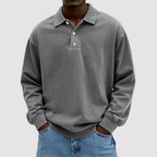 Close front view of a grey vintage-wash long-sleeve polo top showing dropped shoulder seams and ribbed cuffs