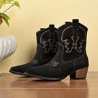 Side profile of a black suede western ankle boot with contrast stitching and tan stacked heel, worn on a model