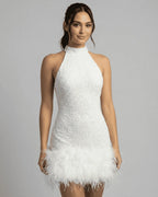Front view of a model wearing a white sequin halter mini dress with a feathered hem against a grey studio backdrop