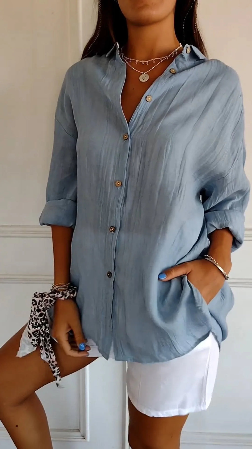 Front view of the blue linen shirt with sleeves rolled up, showing the relaxed fit and curved hem over white shorts
