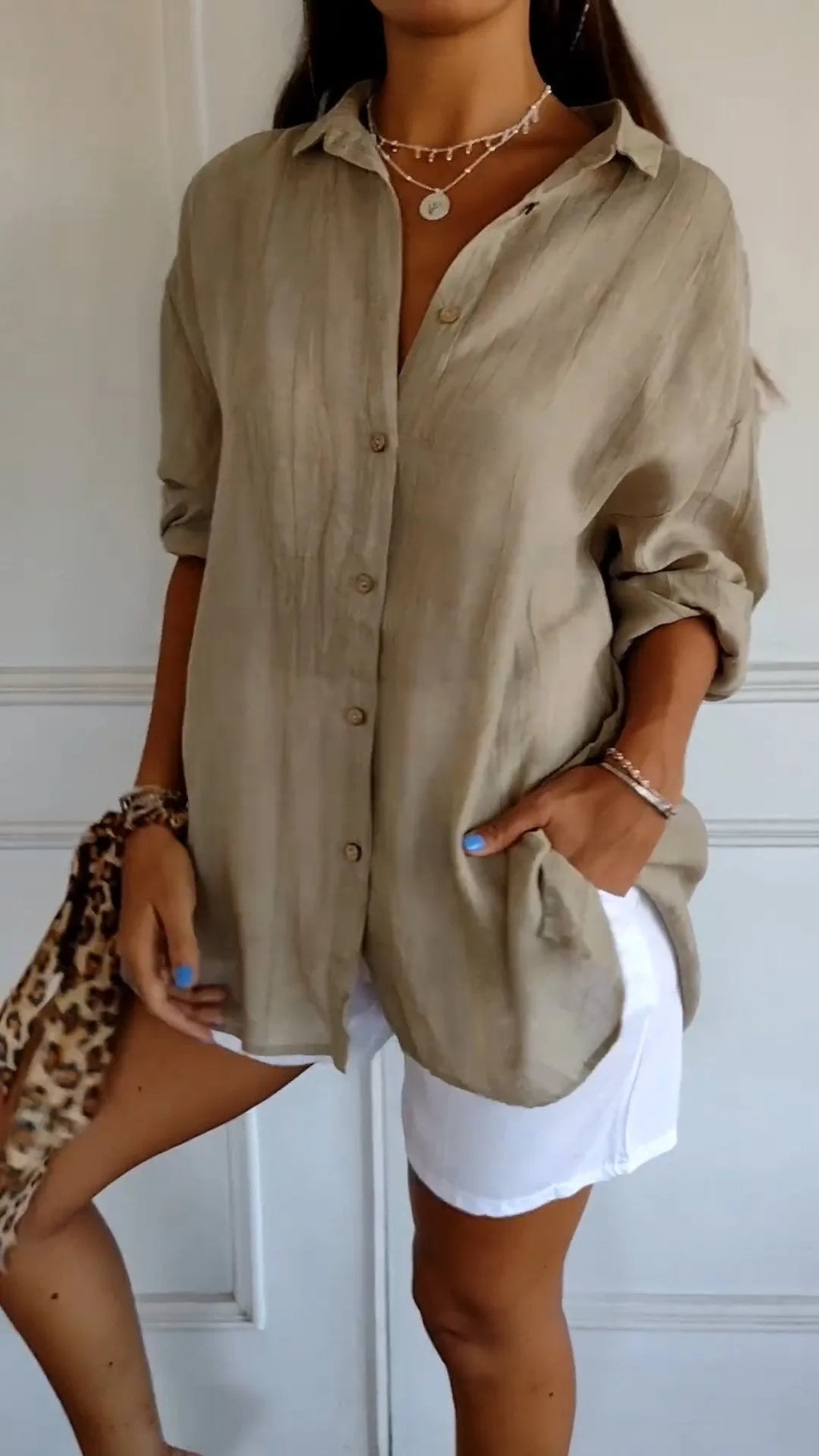 Beige linen shirt buttoned to the chest, worn with sleeves rolled and tucked loosely into white shorts