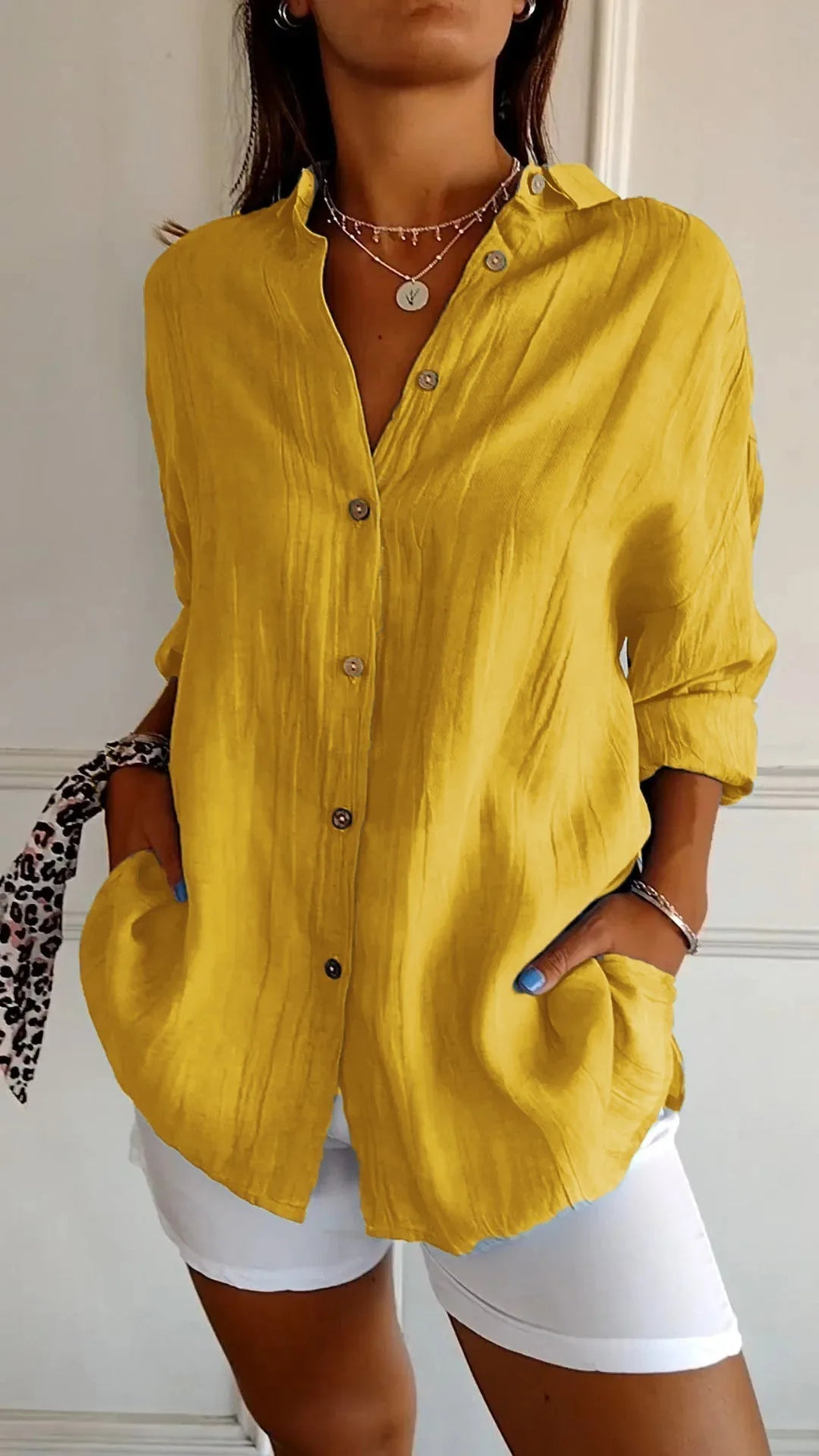 Mustard yellow linen shirt with open V-neck collar, long sleeves rolled, paired with white shorts