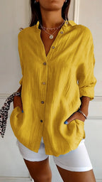 Mustard yellow linen shirt with open V-neck collar, long sleeves rolled, paired with white shorts