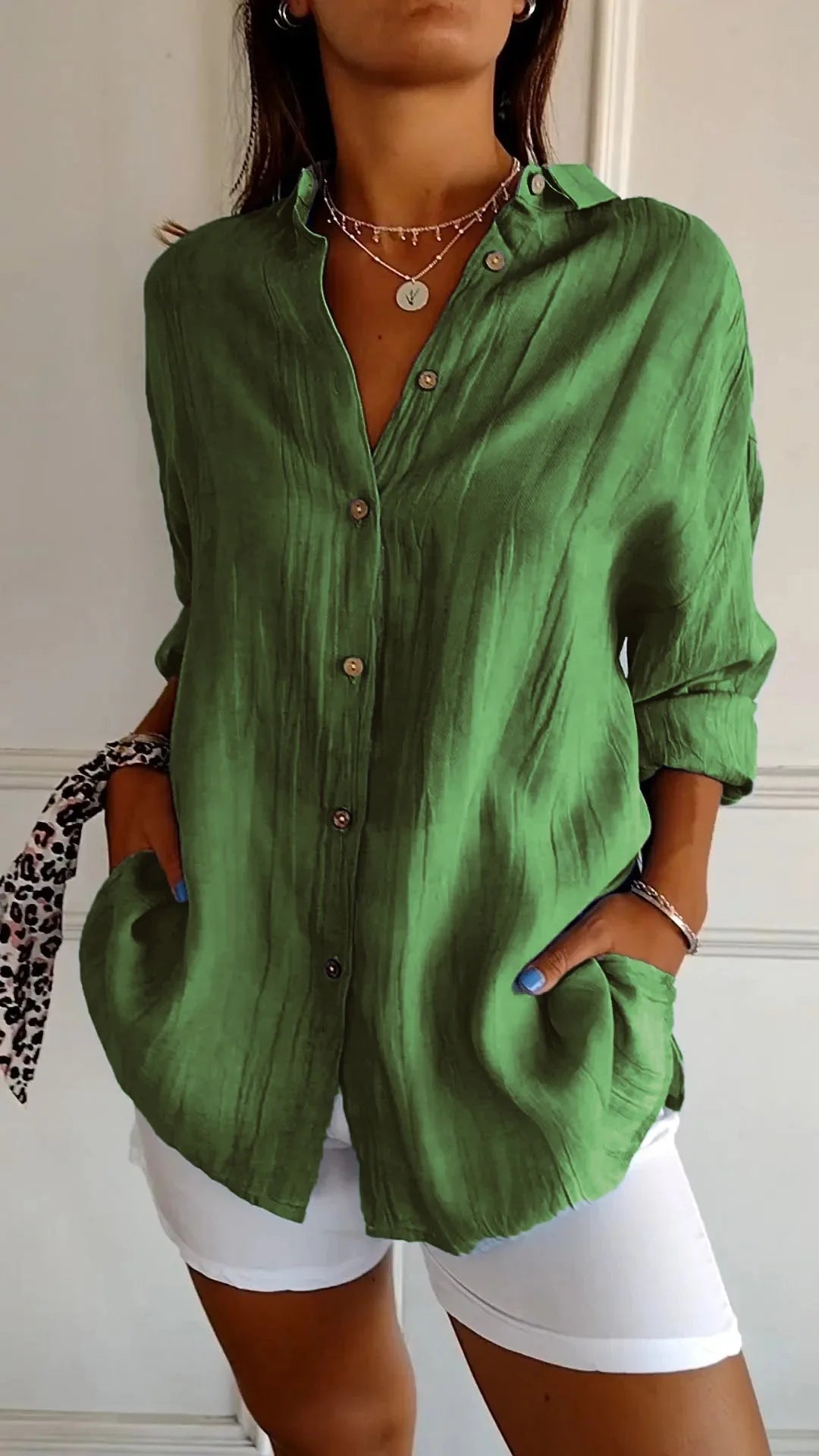 Bright green linen shirt with pointed collar and curved hem, styled over white shorts with gold jewellery