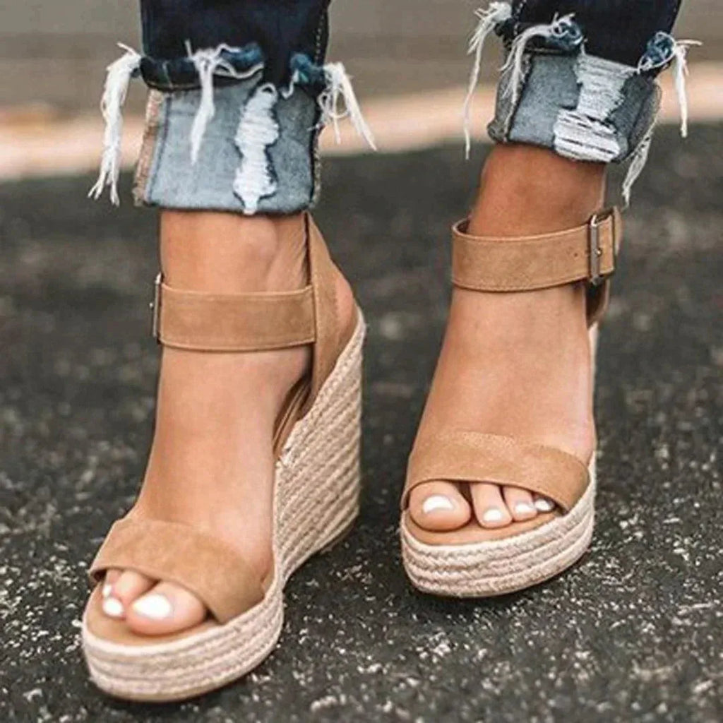 Close-up of woven tan espadrille wedge sandals with ankle strap buckle, worn with rolled distressed denim jeans