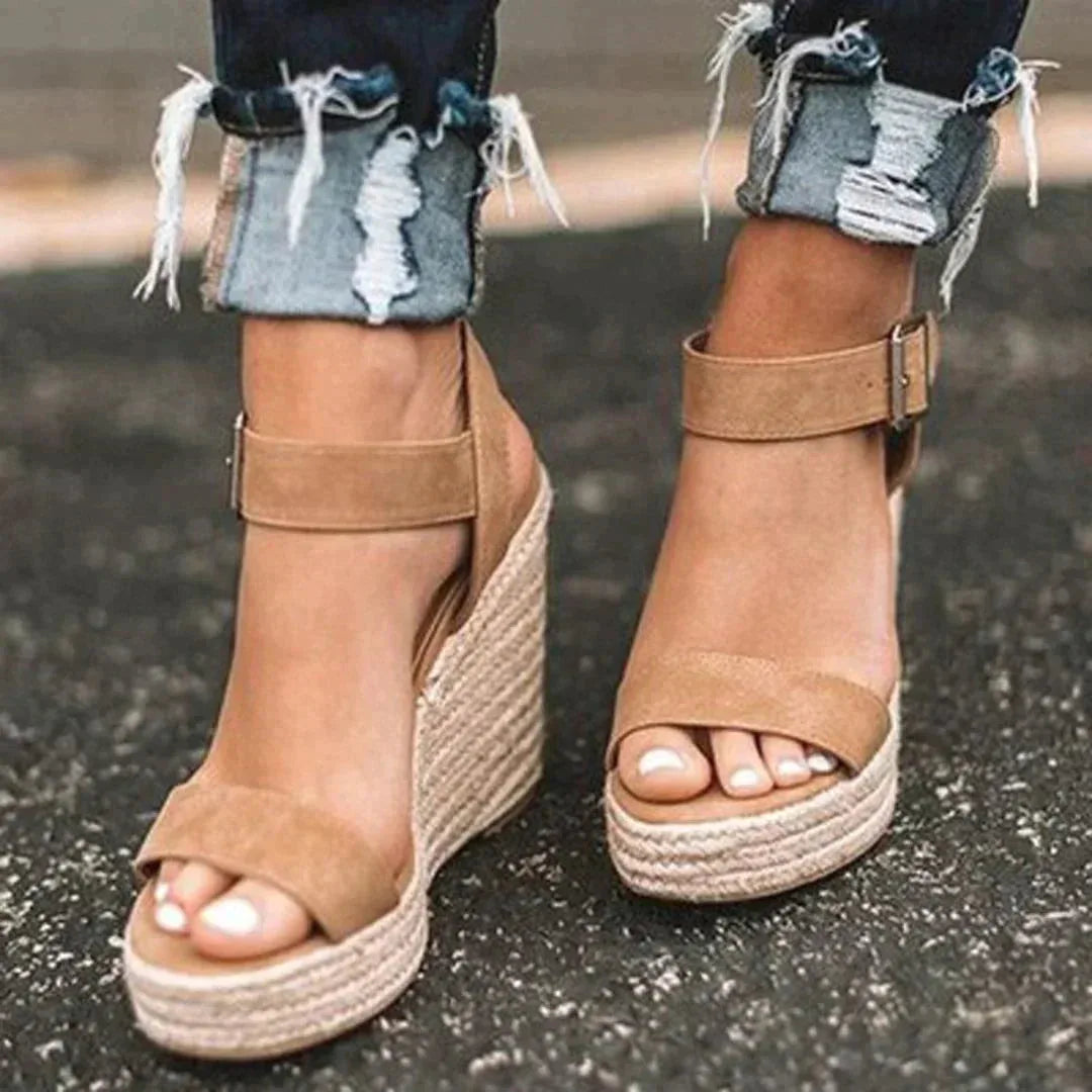 Close-up of woven tan espadrille wedge sandals with ankle strap buckle, worn with rolled distressed denim jeans