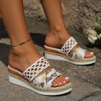 Side profile of black lattice-woven strap sandal with shimmering dark vamp on a light wooden floor background