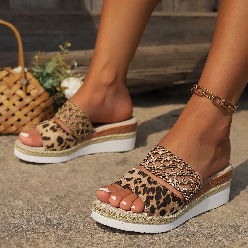 Angled close-up of leopard print sandal with gold woven ankle strap, worn with a gold chain anklet