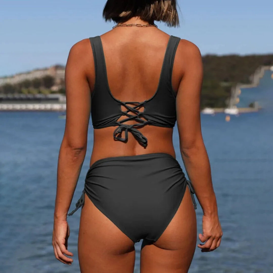 Back view of the black bikini showing wide shoulder straps and a crisscross lace-up tie detail below the shoulder blades