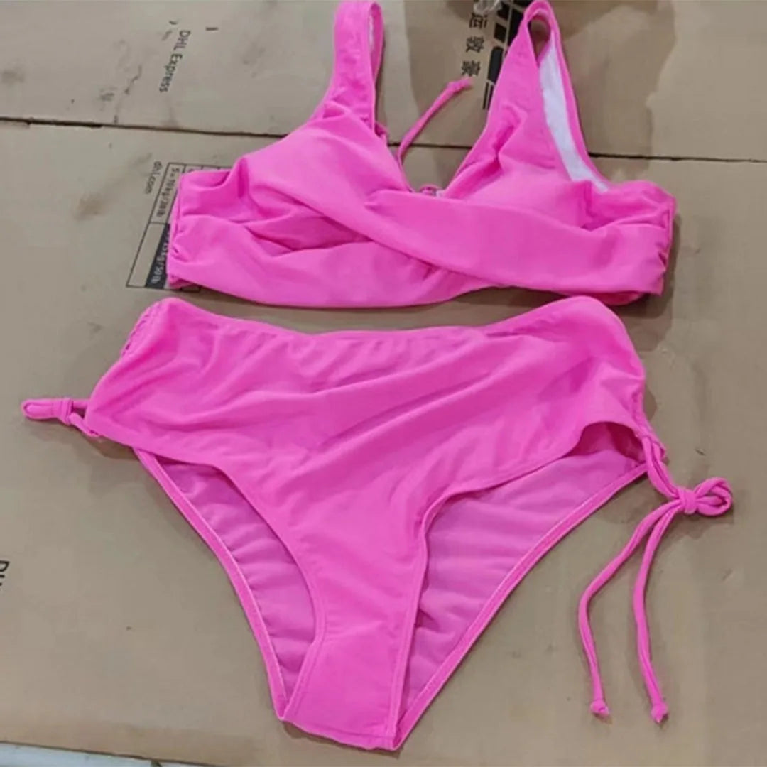 Flat lay of a hot pink bikini set showing the wrap top and high-waisted bottoms with tie-side ruching detail
